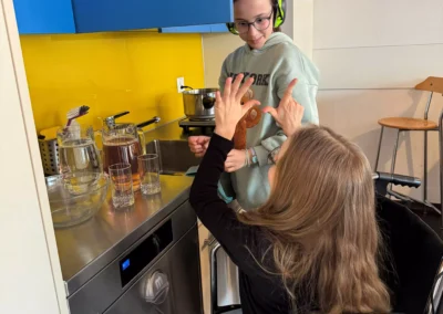 Eine Schülerin im Rollstuhl versucht mit Gebärden ihrer Kollegin mit den Kopfhörern etwas zu sagen.