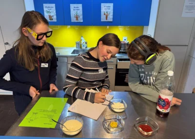 Drei Schülerinnen besprechen das Menü. Eine trägt Kopfhörer, die andere eine Kartonbrille.