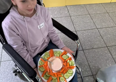 Eine Schülerin im Rollstuhl mit einem gefüllten Teller auf den Knien
